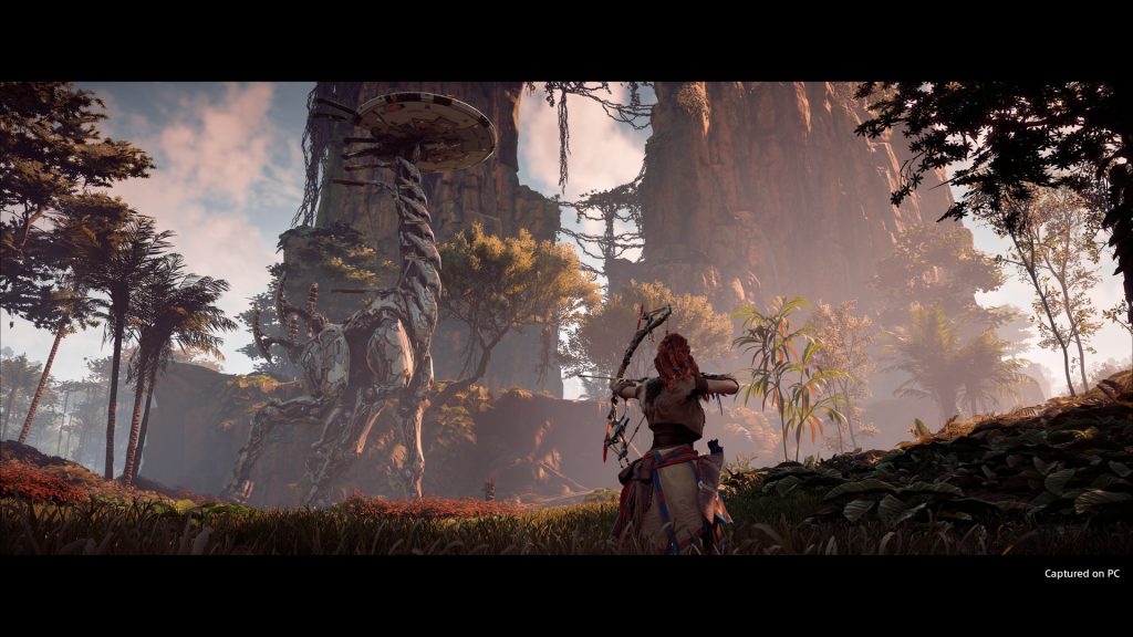 Aloy facing a large machine in a wooded landscape in Horizon Zero Dawn.